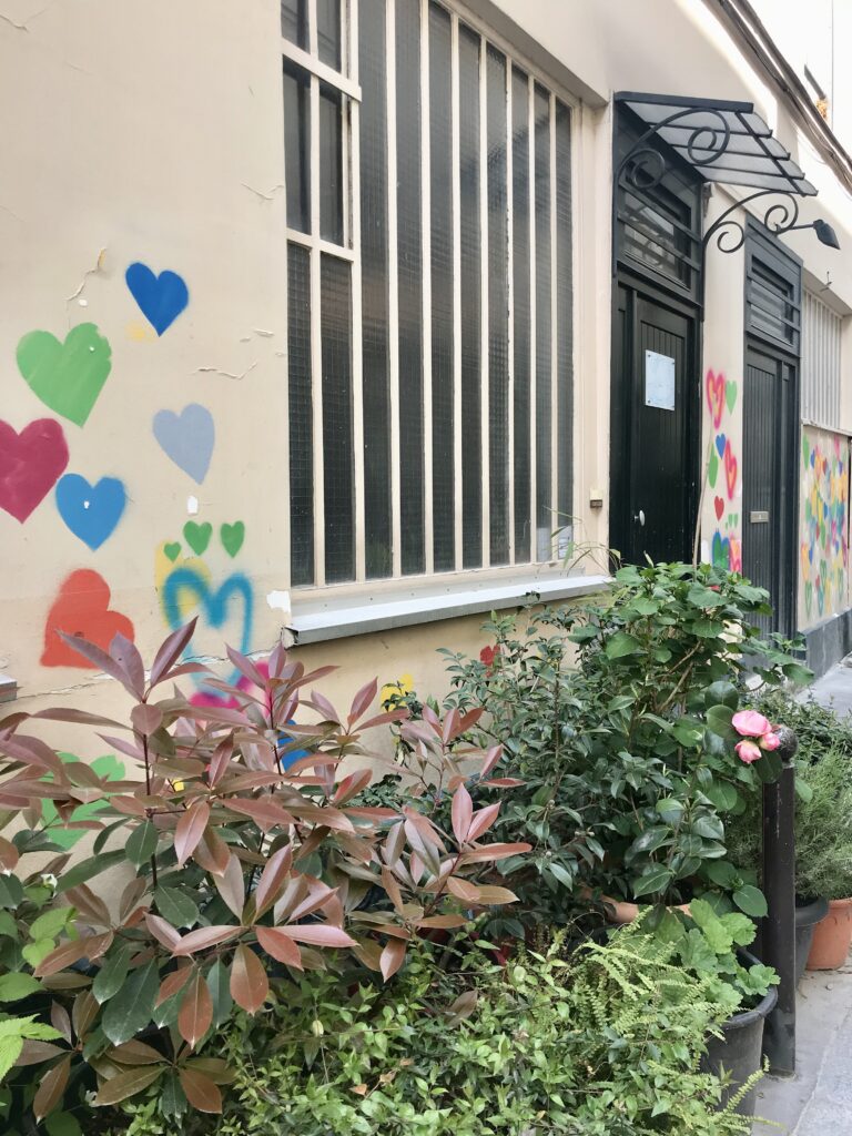 Colorful Paris street Cité Dupont with heart graffiti, leafy plants, and black doors under decorative iron awnings